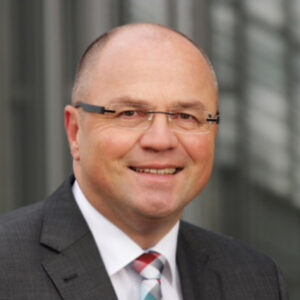 Eine Person mit Brille und Anzug lächelt in die Kamera.