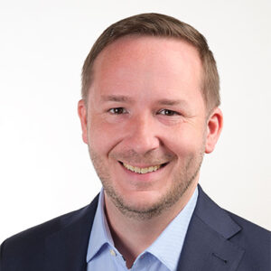 Ein Mann in Anzug und Hemd lächelt in die Kamera.