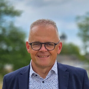Mann mit Brille und Anzug hört im Freien. Hintergrund unscharf.