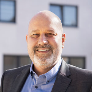 Ein lächelnder Mann im Anzug im Freien vor einem Gebäude.