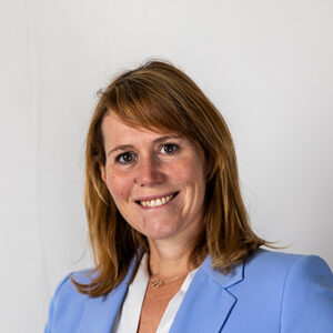 Eine lächelnde Frau in einem blauen Blazer vor weißem Hintergrund.