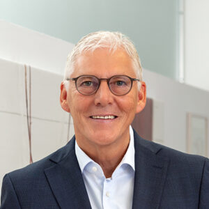 Älterer Mann mit Brille in Anzug, lächelt in die Kamera.