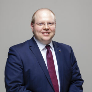 Mann in Anzug mit roter Krawatte vor grauem Hintergrund.