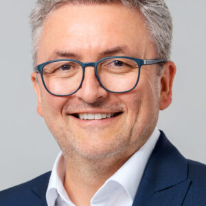 Mann mit Brille und Anzug lächelt in die Kamera.