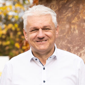 Älterer Mann mit weißem Hemd lächelt, Hintergrund mit Herbstlaub.