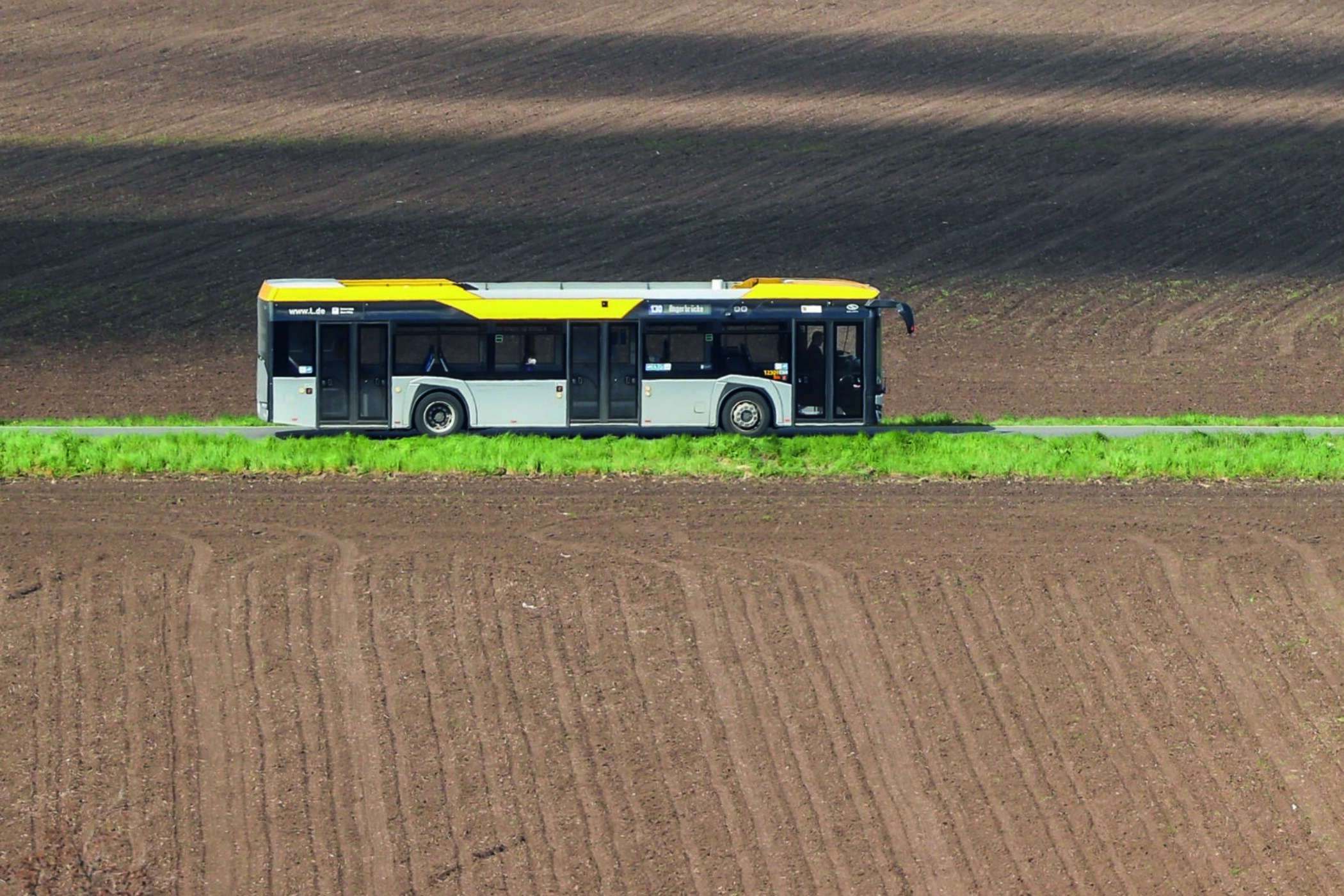 Ein Linienbus fährt entlang eines Feldwegs