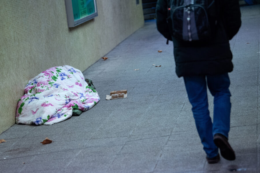 Ein Wohnungsloser liegt mit einer Decke auf dem Fußweg