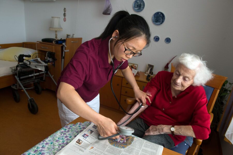 Die chinesische Pflegekraft Linyan Liu (l) misst in der Seniorenwohnanlage Ludwigstift am 11.02.2015 in Stuttgart (Baden-Württemberg) einer Bewohnerin den Blutdruck. Mit einem Pilotprojekt hat der Arbeitgeberverband Pflege zunächst 27 Krankenschwestern aus China nach Baden-Württemberg geholt, die im Südwesten eine Weiterbildung zu Altenpflegerinnen erhalten. Foto: Marijan Murat/dpa (zu dpa "Chinesische Altenpflegerinnen sollen Fachkräftemangel lindern" vom 11.02.2015)