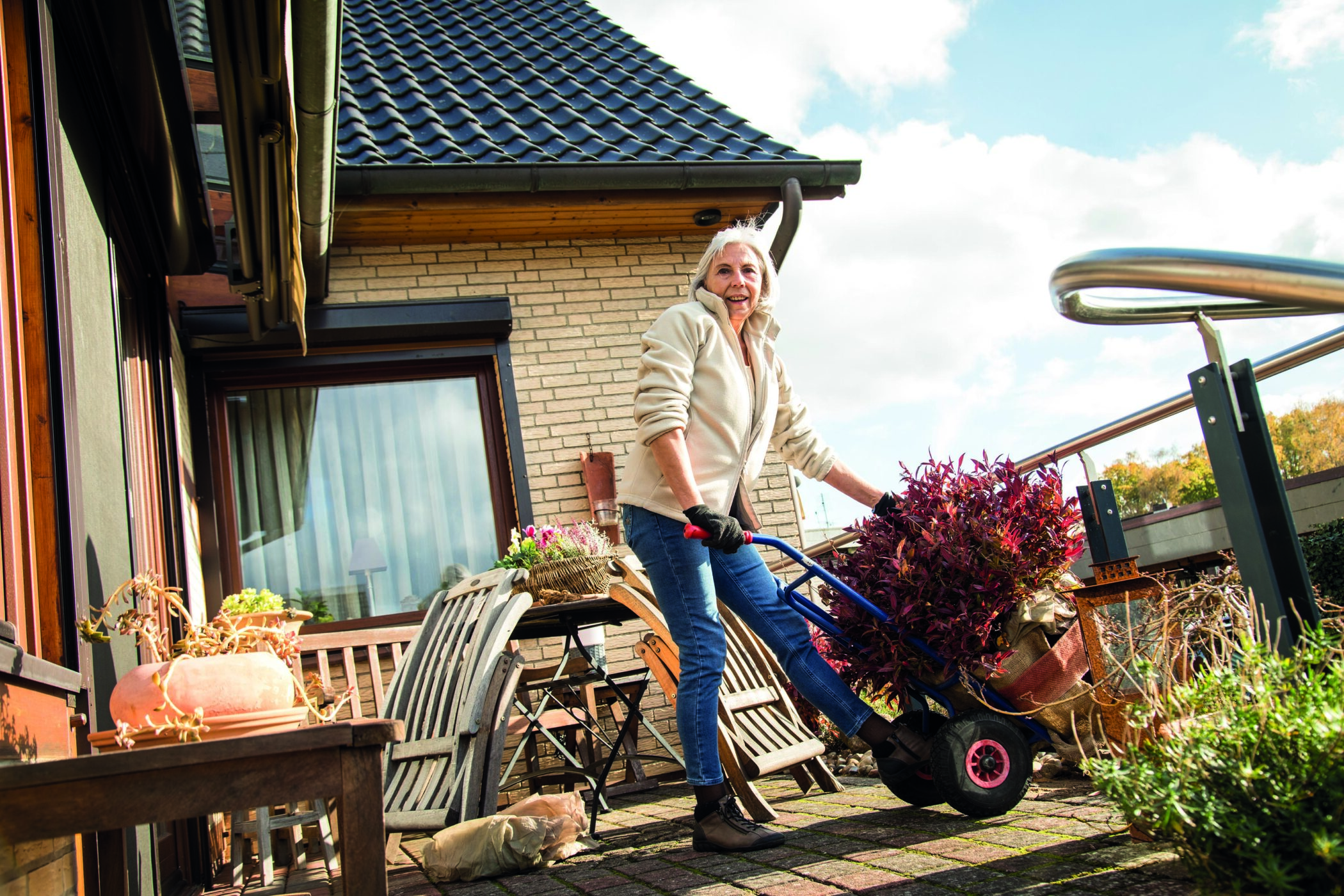 Eine ältere Dame stellt in einem Garten einen Pflanzentopf mit einer Sackkarre um