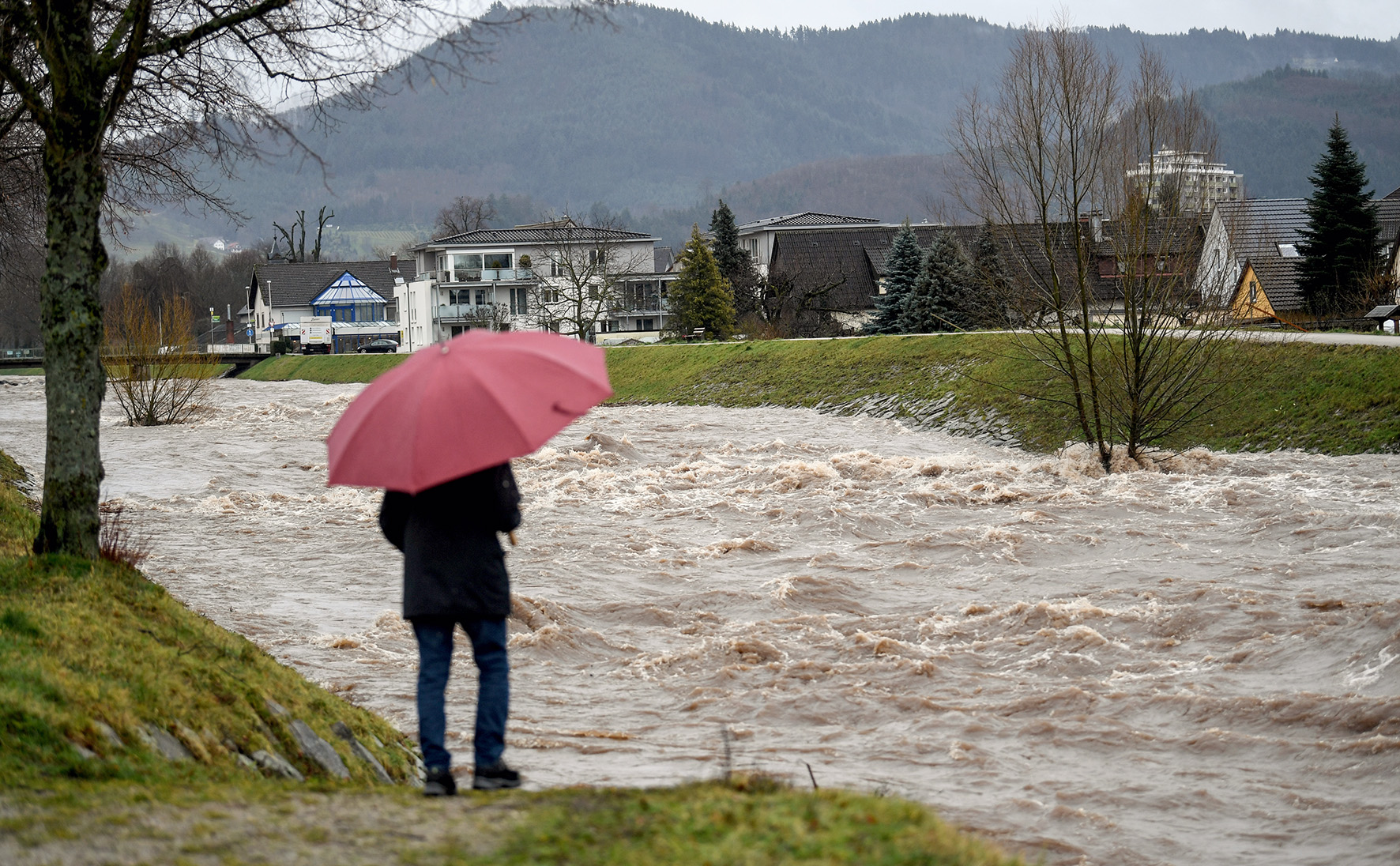 Person mit Schirm vor überfluteter Straße