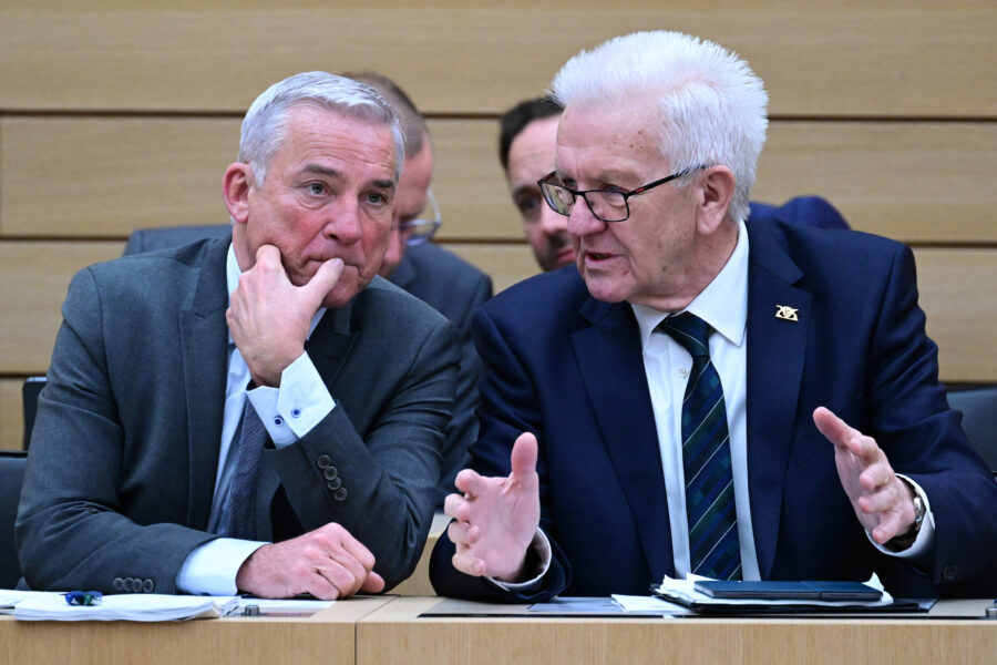 Thomas Strobl (l, CDU), Innenminister von Baden-Württemberg, und Winfried Kretschmann (Bündnis 90/Die Grünen), Ministerpräsident von Baden-Württemberg, unterhalten sich bei einer Landtagsdebatte im Plenarsaal.