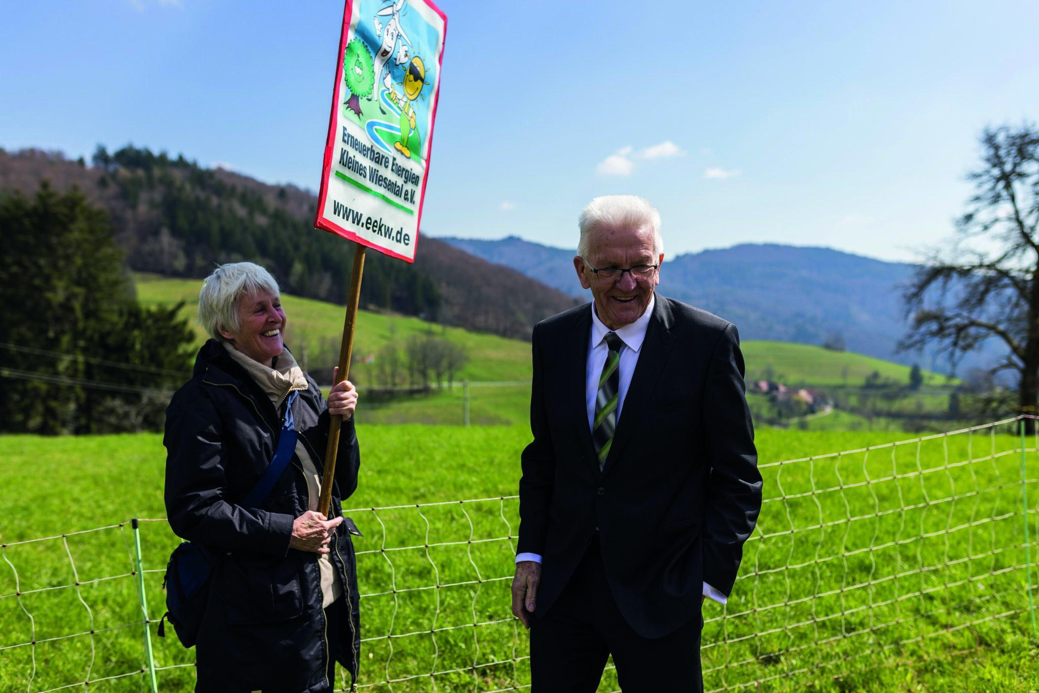 Ministerpräsident Winfried Kretschmann steht vor der Kapelle der Ortschaft Ried und spricht mit einer Windkraftbefürworterin