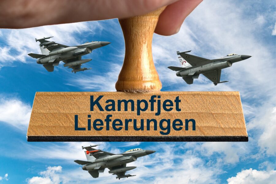 Ein symbolischer Holzstempel mit der Aufschrift "Kampfjet Lieferungen", gehalten von einer Hand, vor einem blauen Himmel mit Schleierwolken und drei F16 Kampfjets.