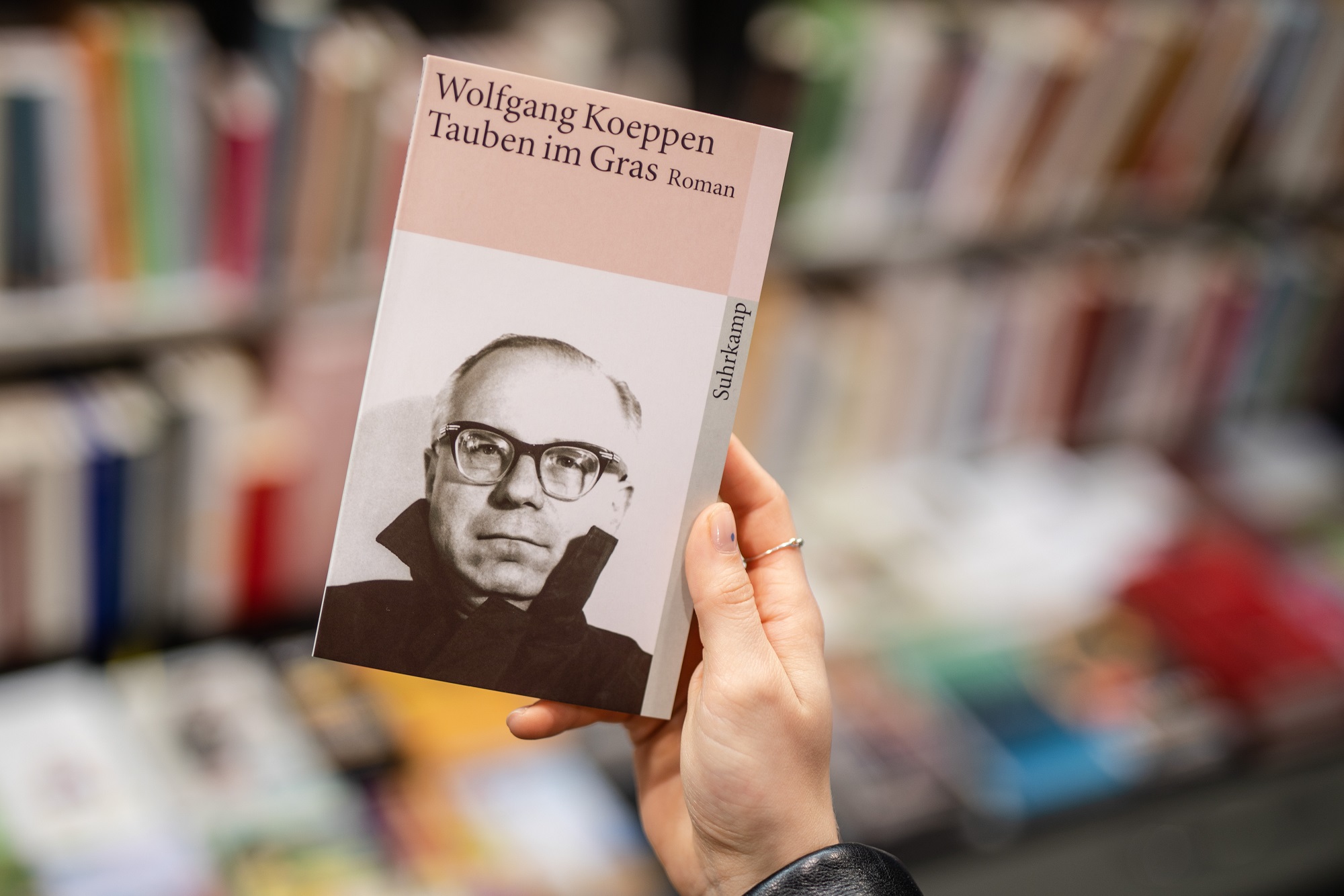Eine Frau hält in einer Buchhandlung das Buch «„Tauben im Gras»“ von Wolfgang Koeppen in ihrer Hand.