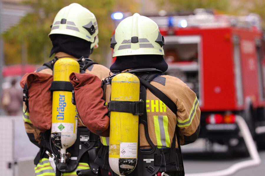 Feuerwehrmänner mit Atemschutz, Helm und Druckluftflaschen von hinten am Einsatzort.