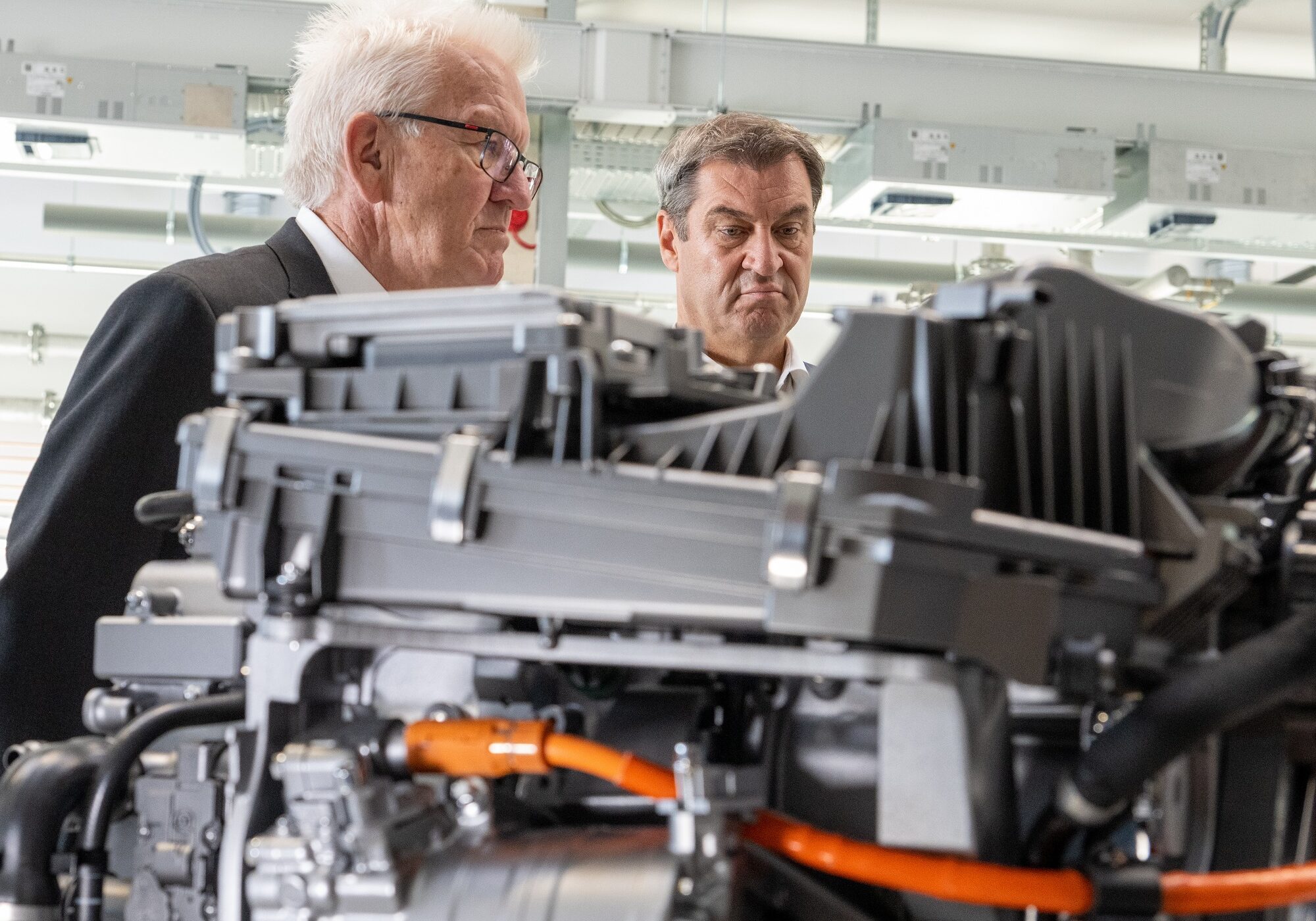 Winfried Kretschmann und Markus Söder stehen im Zentrum für Sonnenenergie- und Wasserstoff-Forschung hinter einem Brennzellenmotor.