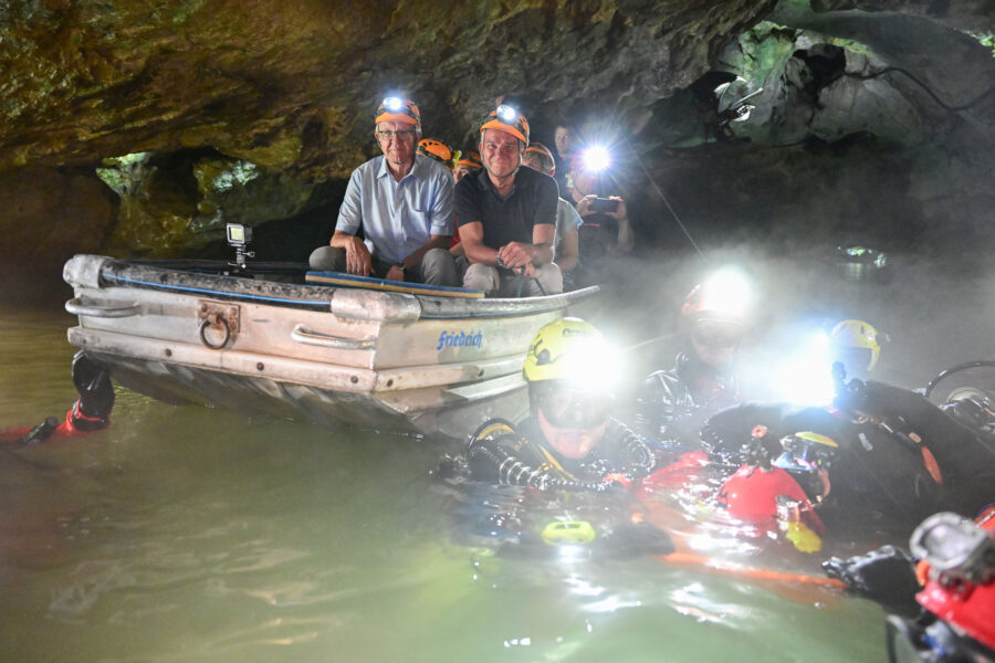 Ministerpräsident Kretschmann und Innenminister Strobl sitzen in der Wimsener Höhle in einem Boot, um einem Rettungs-Team bei einer Vorführung einer Höhlenrettung zuzusehen.