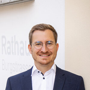 Ein Mann mit Brille in Anzug vor einer weißen Wand mit dem Text "Rathaus Burgstrasse".