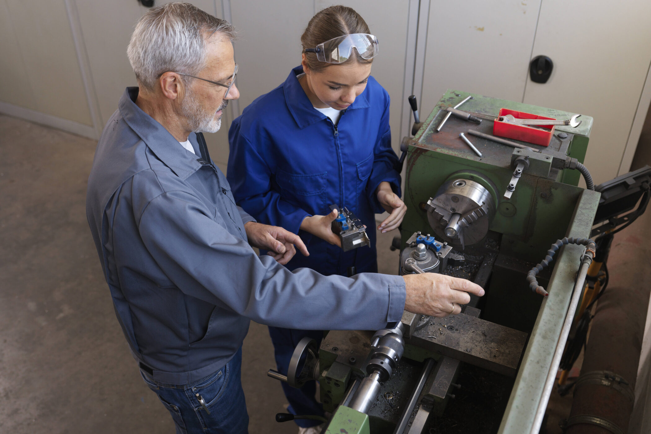 Zwei Personen in Arbeitskleidung an einer Drehmaschine.