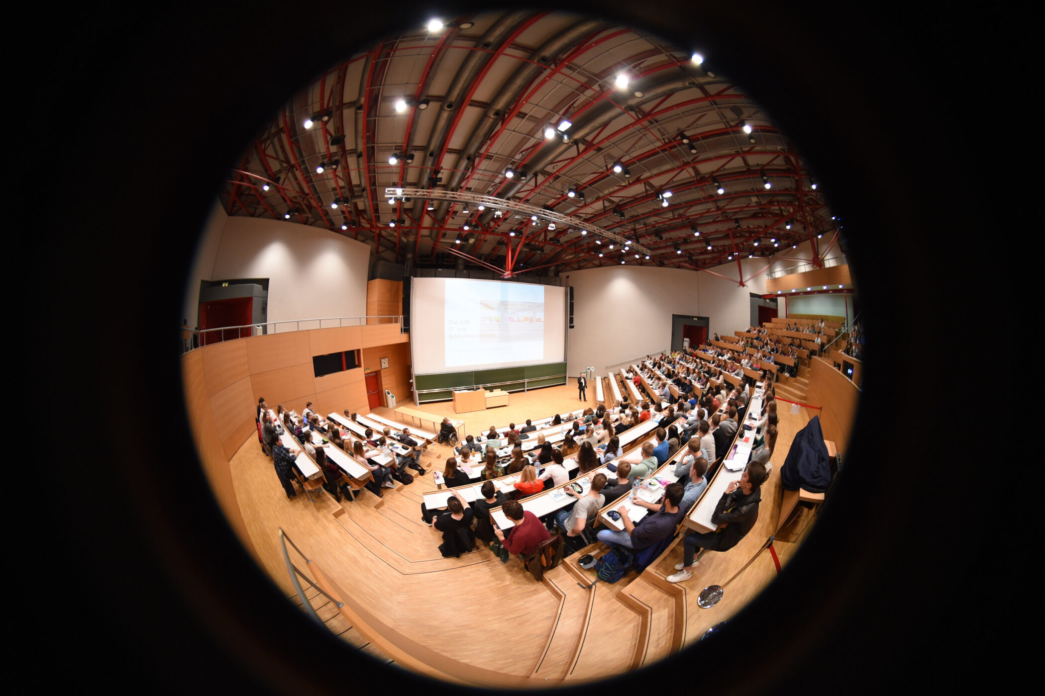 Großer Hörsaal mit vielen Menschen, die einer Präsentation folgen.