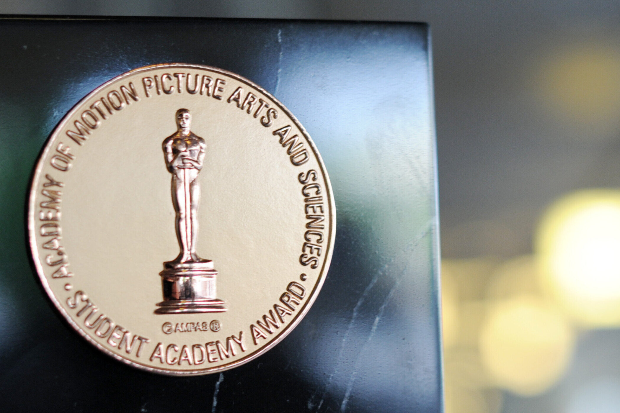 Runde Medaille mit Oscar-Statue und Schriftzug auf schwarzem Hintergrund.