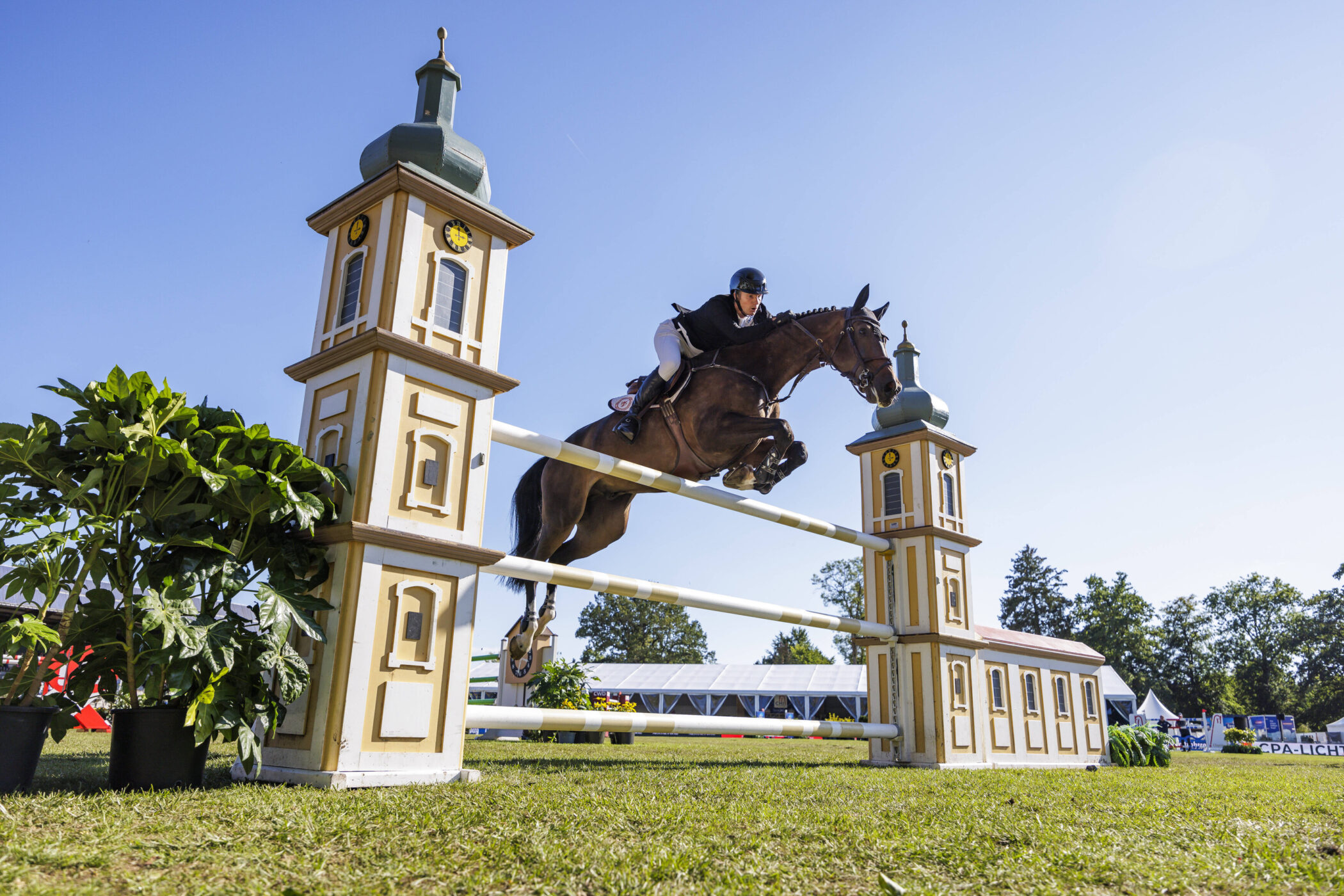 Reiter springt mit Pferd über Hindernis mit Türmen auf Rasenplatz.