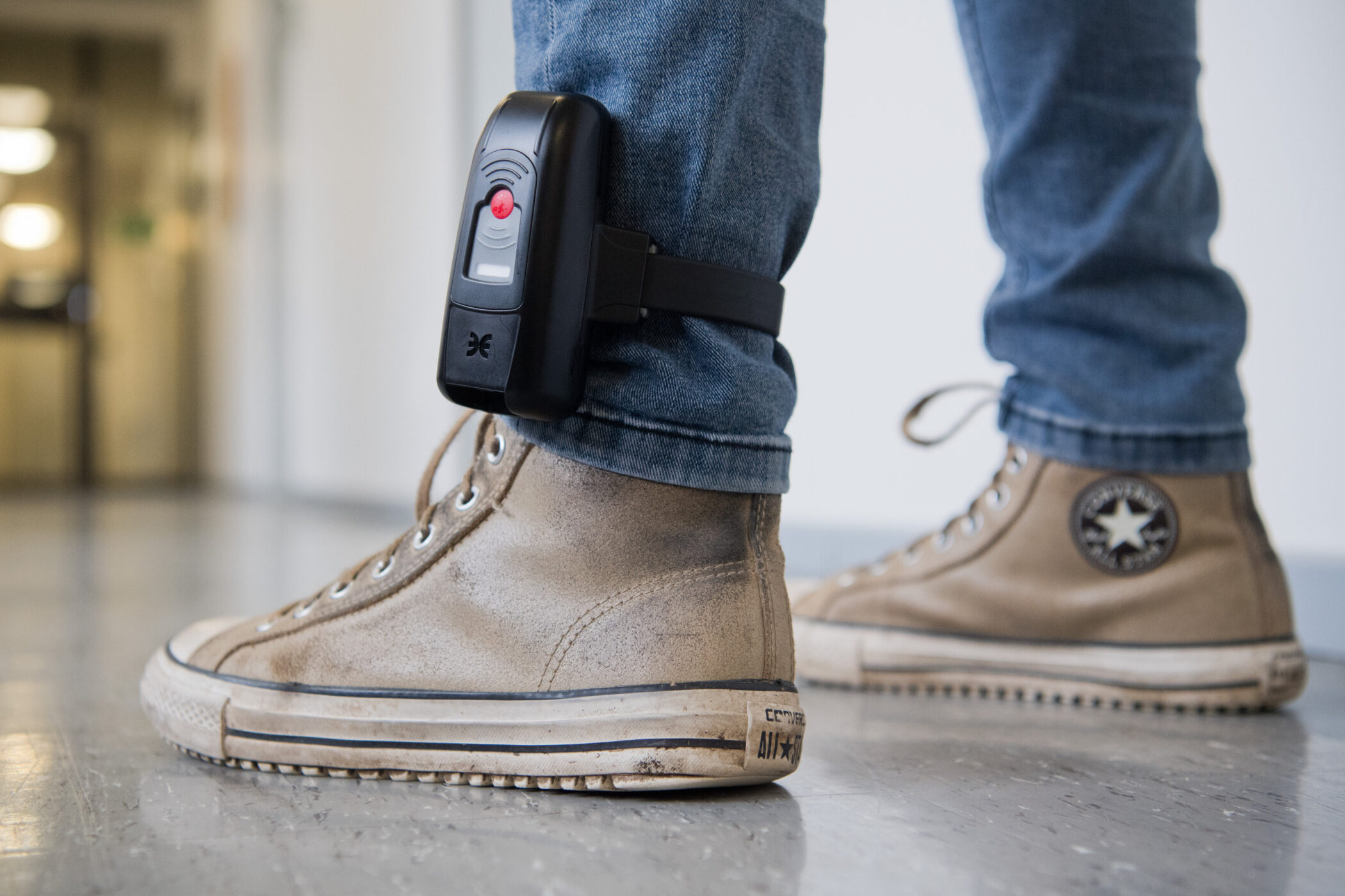 Person trägt elektronische Fußfessel über Jeans und braunen Sneakers.