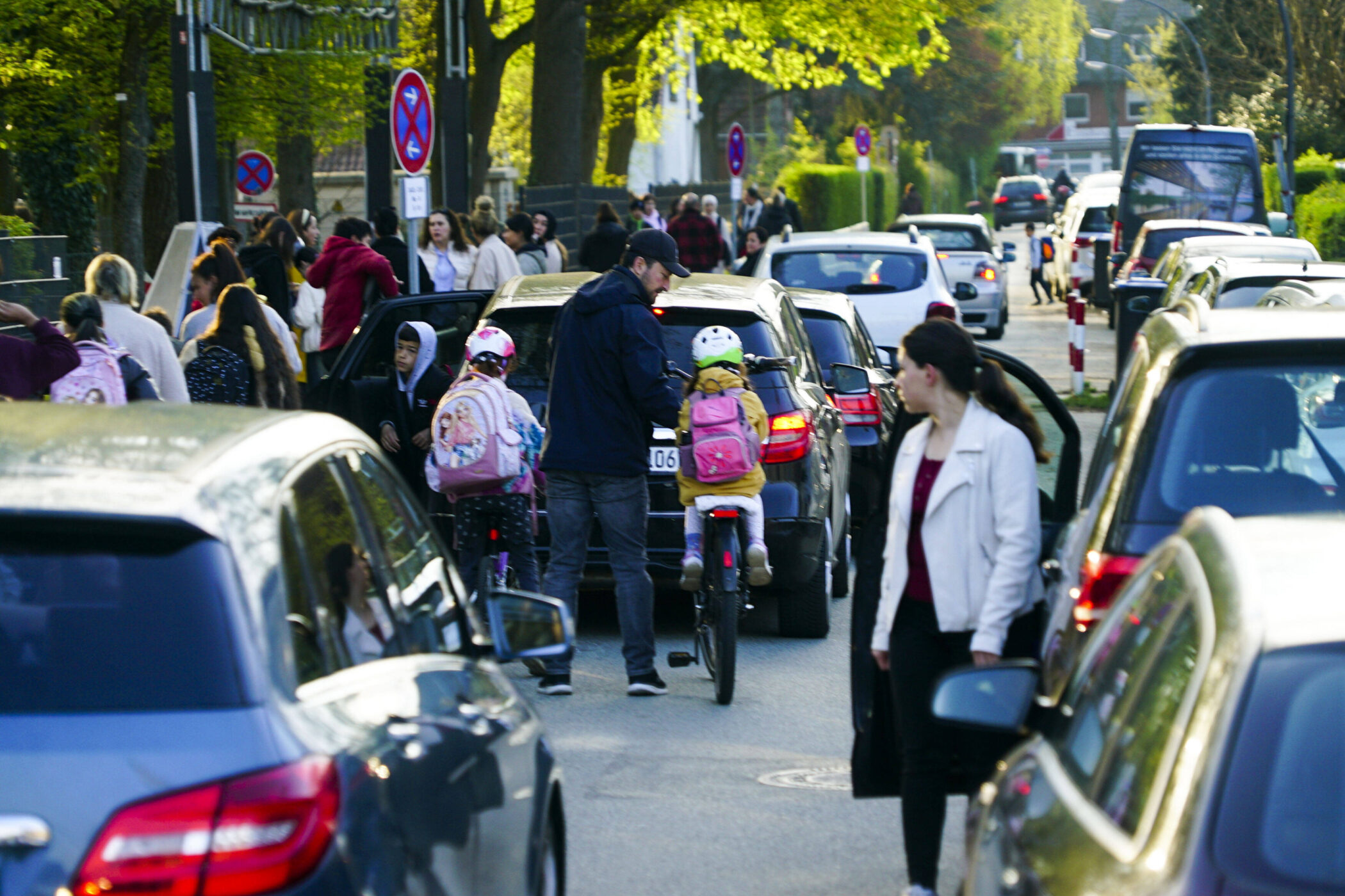 Straße mit vielen Autos, Menschen und Kindern auf Fahrrädern, dichter Verkehr.