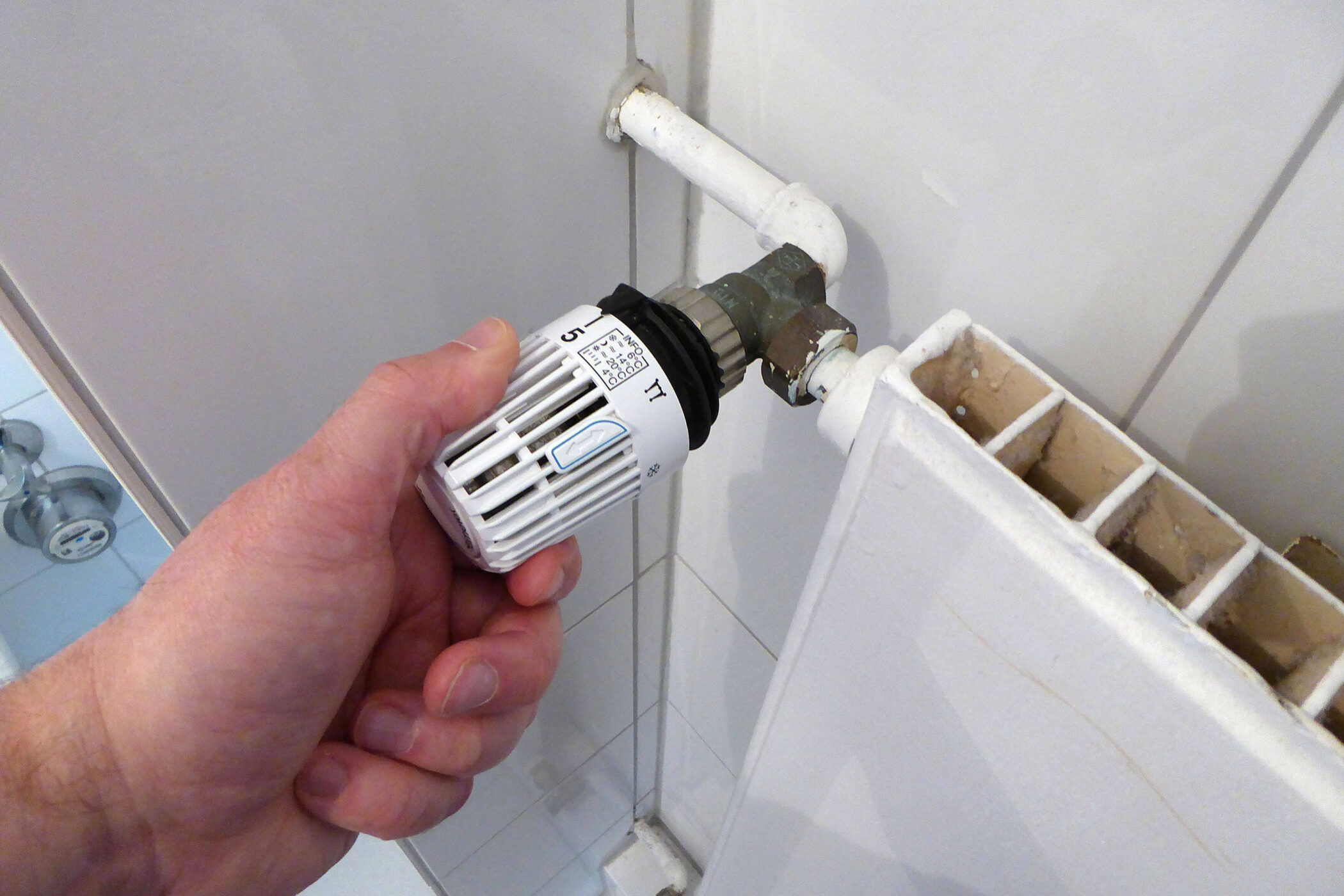 Hand dreht Thermostatventil an einem weißen Heizkörper.
