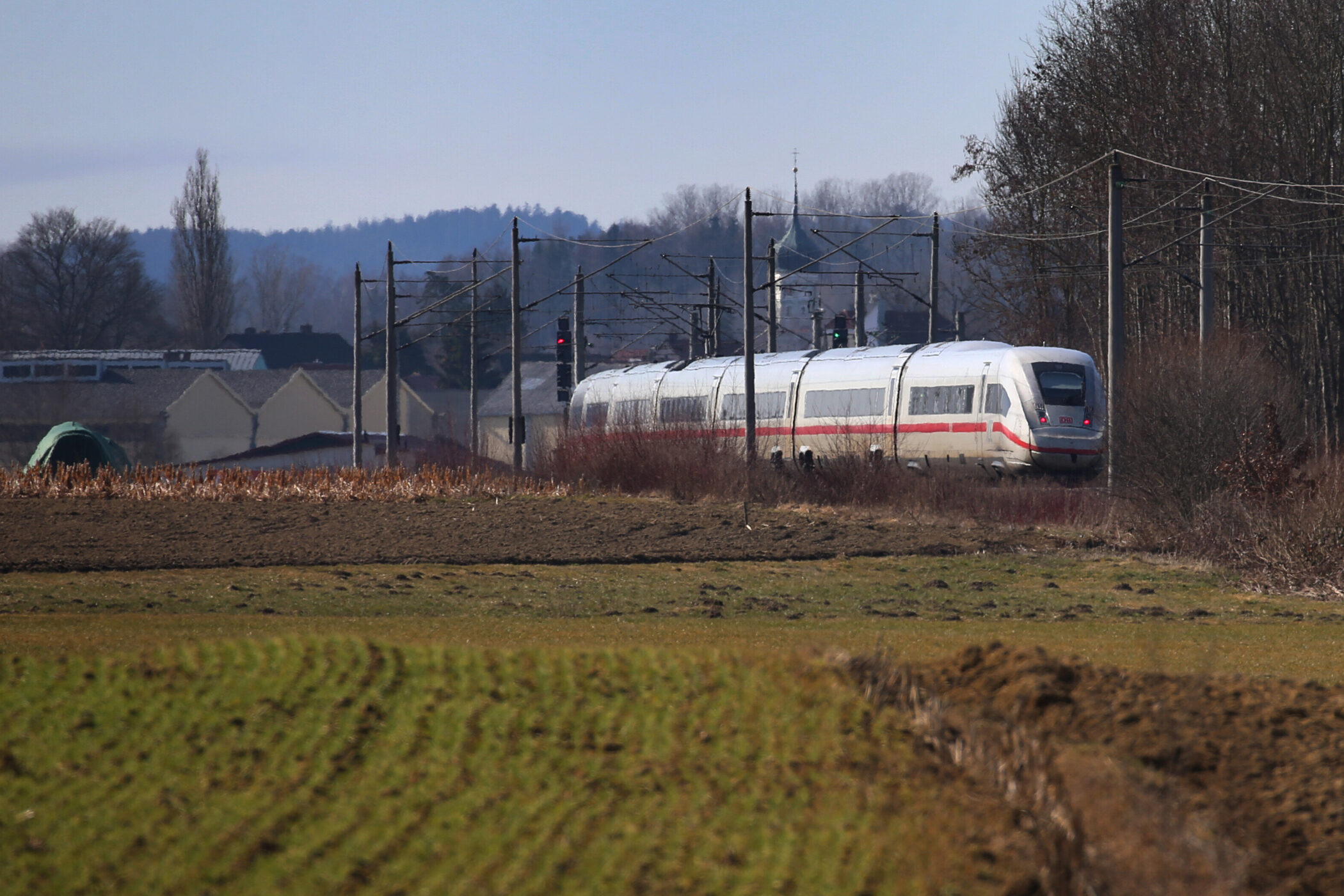 Ein ICE-Zug fährt durch eine ländliche Landschaft mit Feldern und Bäumen.