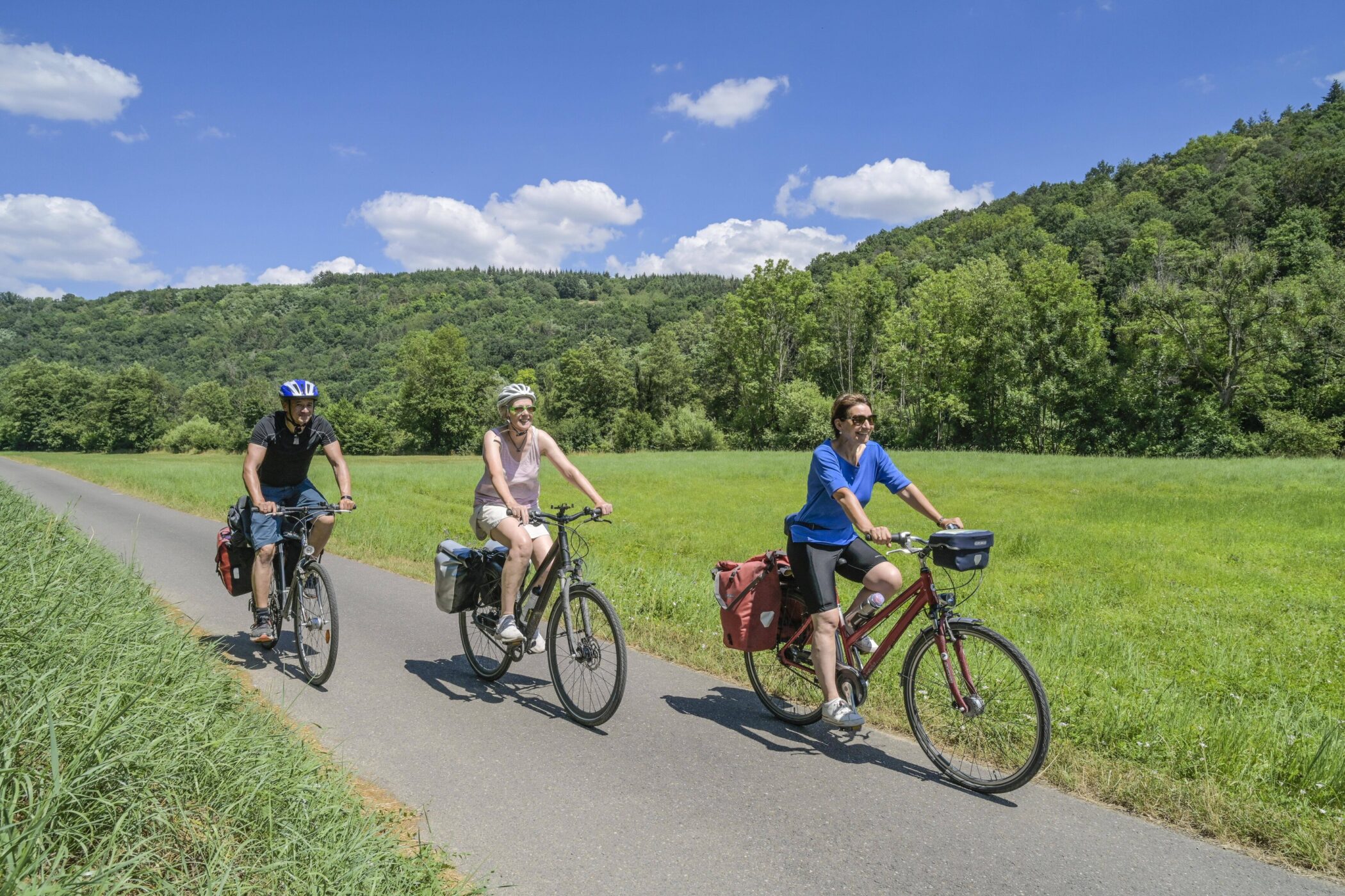 Drei Personen fahren auf Fahrrädern auf einem Weg durch eine grüne Landschaft.