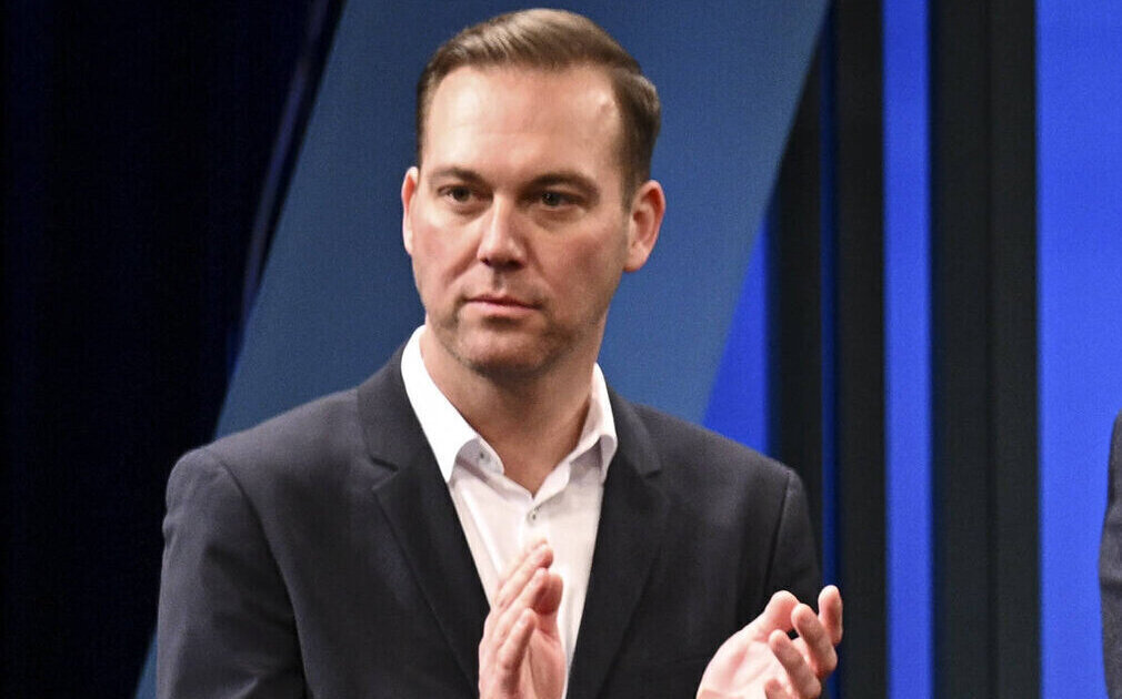 Ein Mann in Anzug klatscht, blauer Hintergrund.