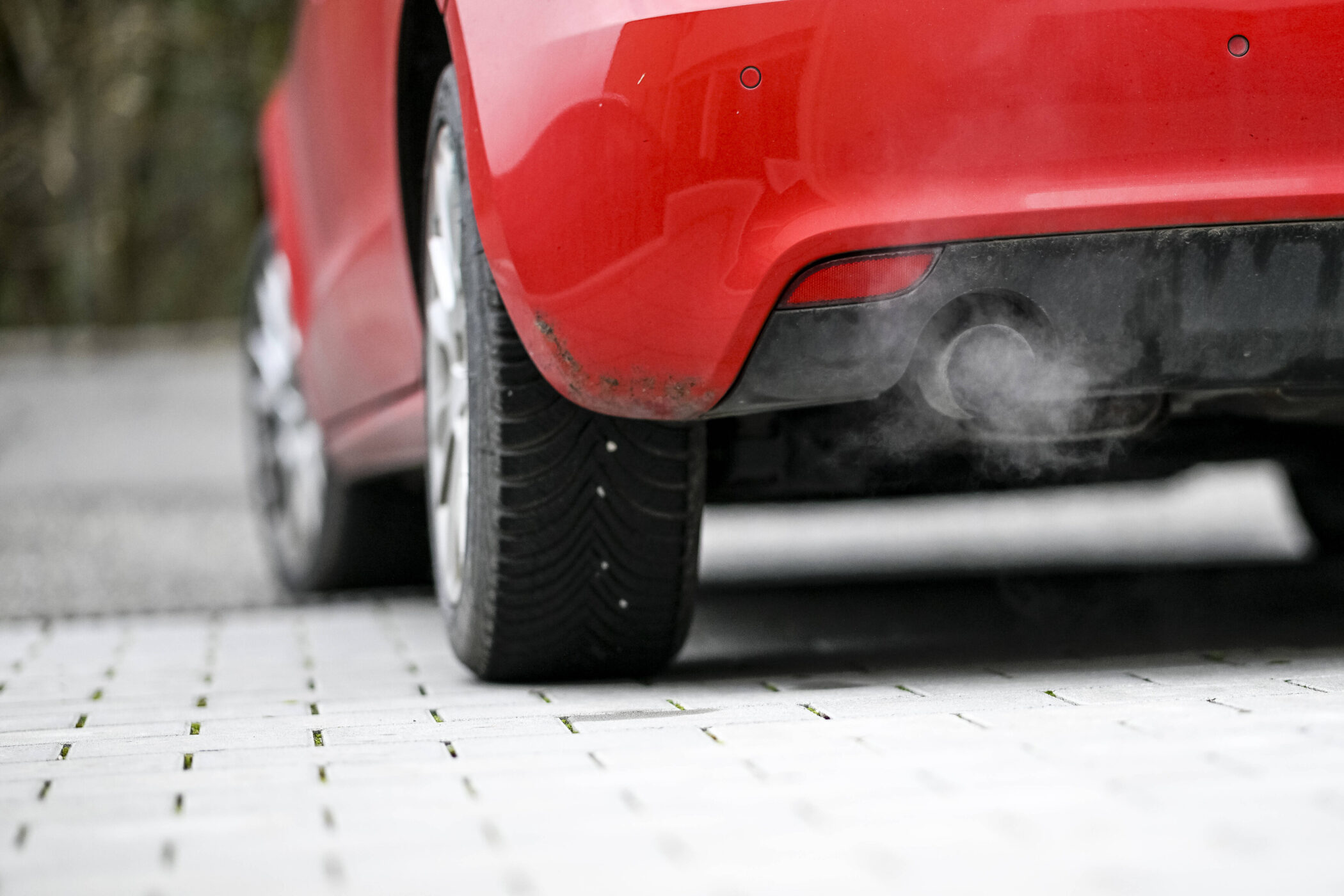 Roter PKW mit Abgasen aus dem Auspuff.