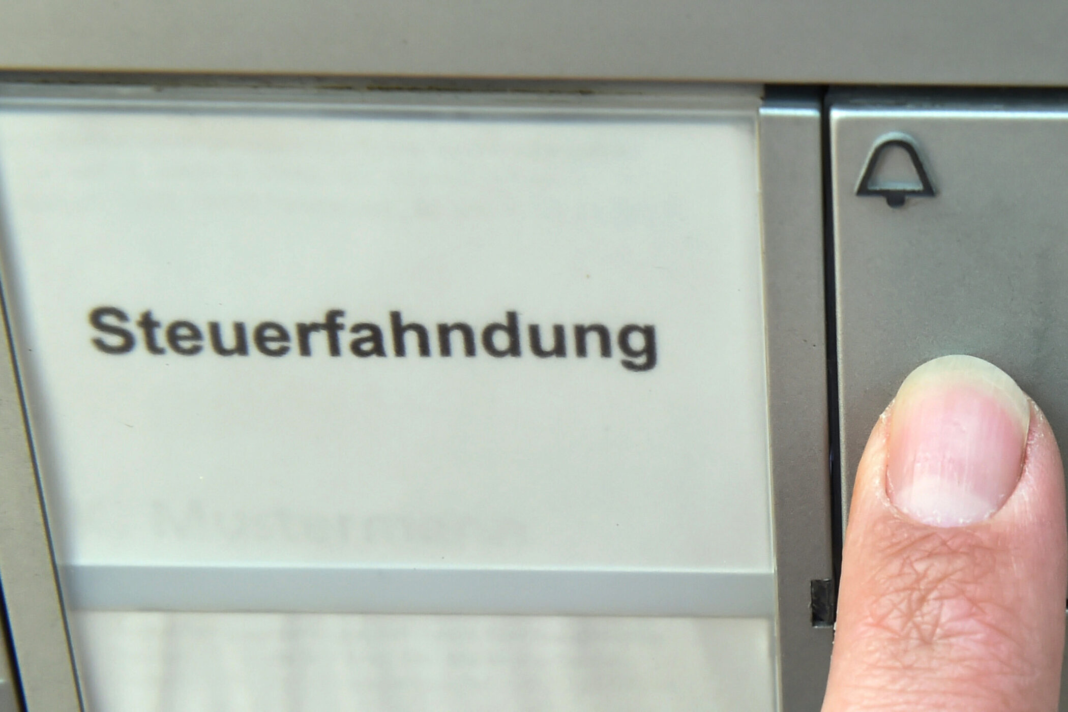 Finger drückt Klingelknopf neben Schild mit Aufschrift "Steuerfahndung".