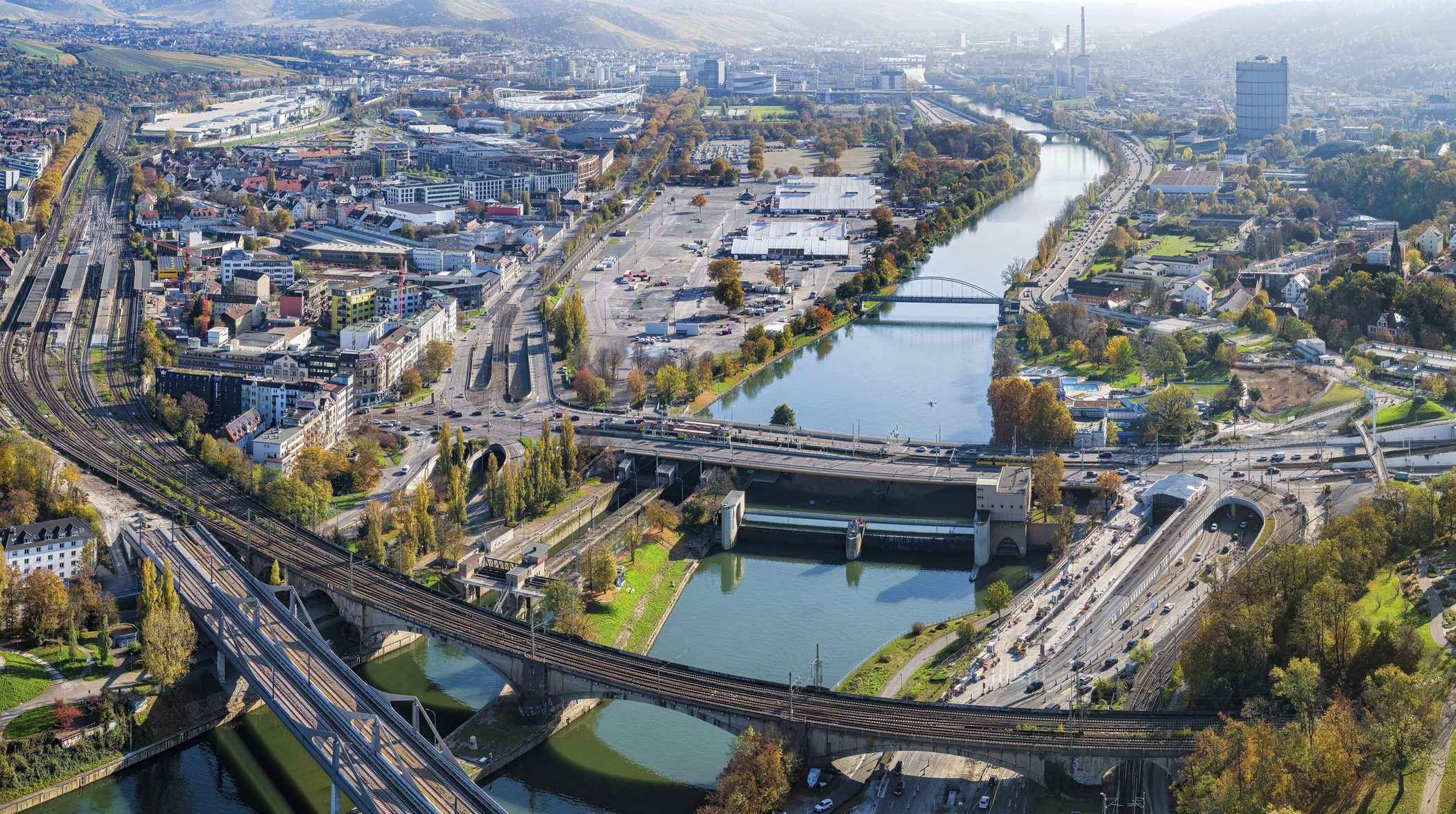 Stadtansicht mit Fluss, Brücken, Straßen und Gebäuden, umgeben von Hügeln und Bäumen.