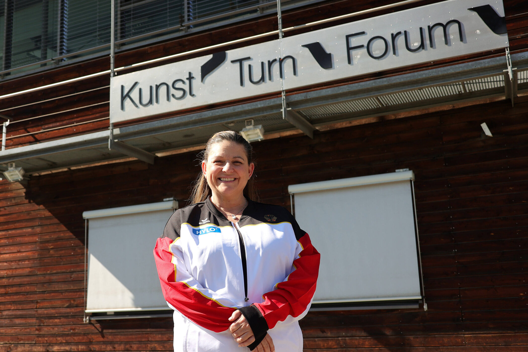 Frau in Sportjacke vor Gebäude mit Schild "Kunst Turn Forum".
