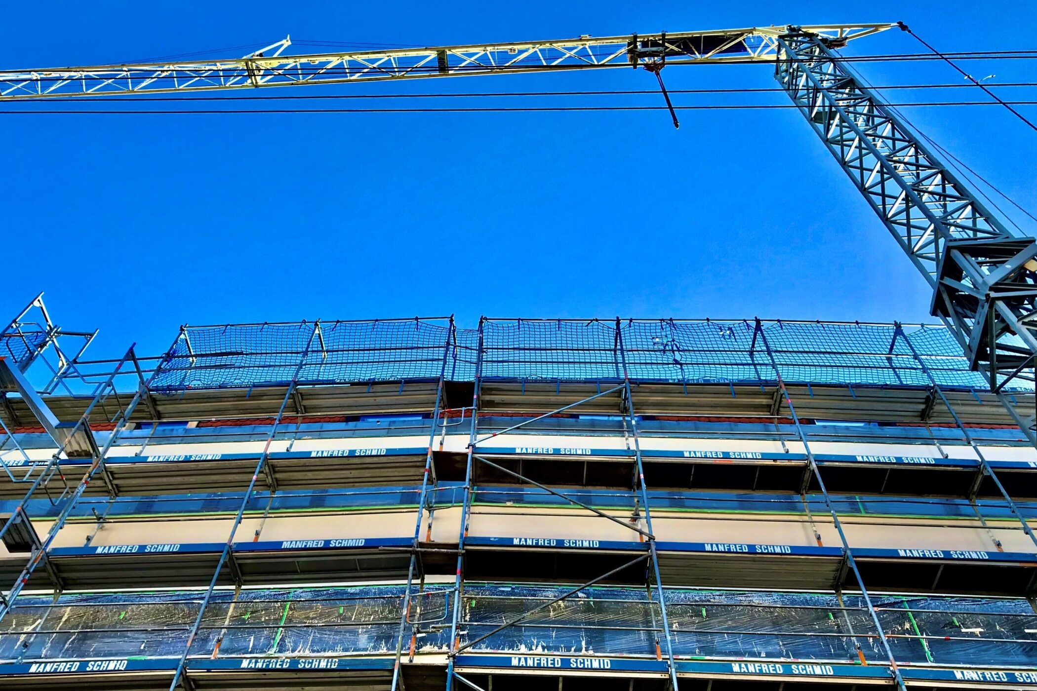 Gerüst und Kran vor blauem Himmel, Schriftzug "MANFRED SCHMID" auf Gerüst.