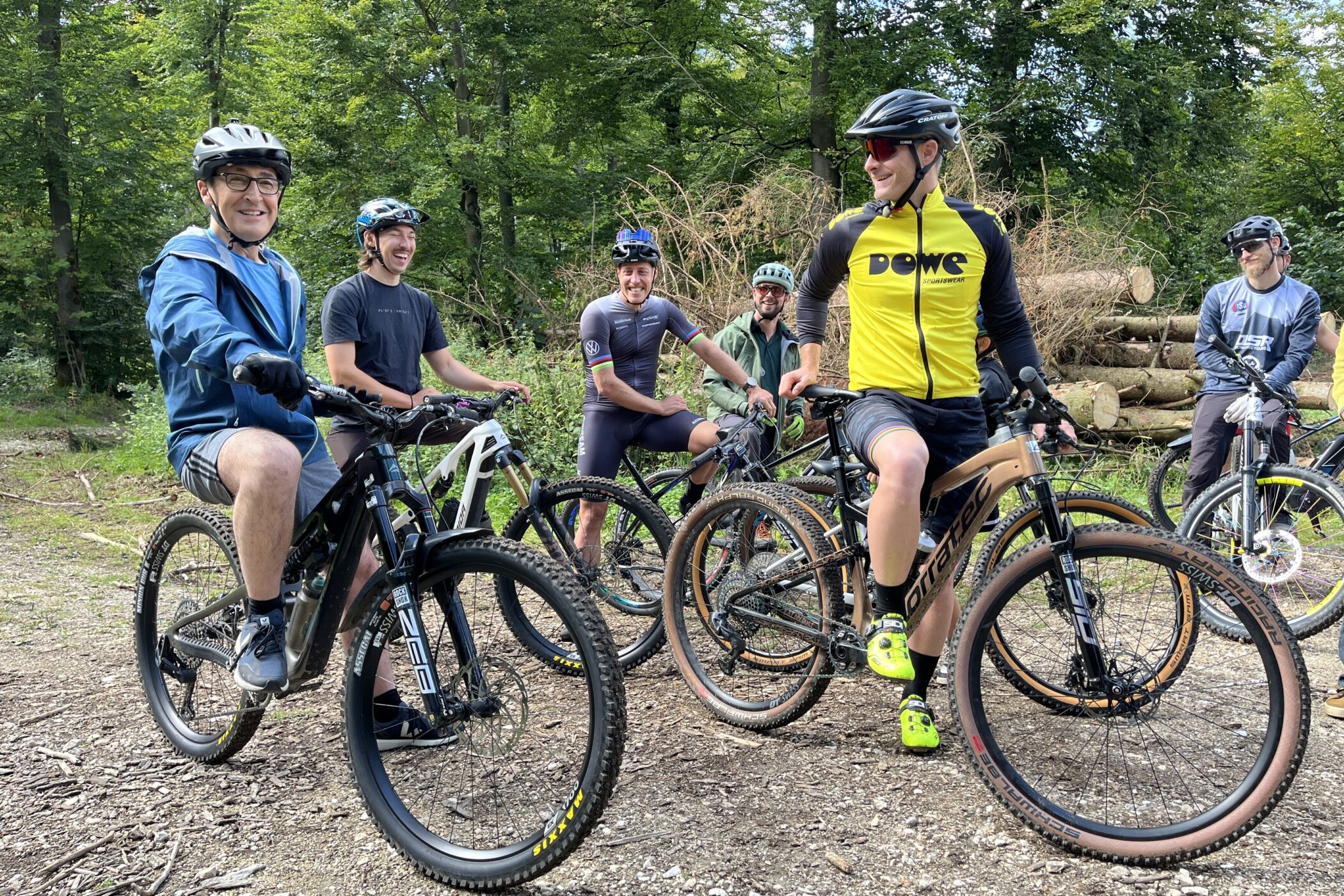 Sechs Personen mit Fahrrädern im Wald, lächelnd und in Sportkleidung.