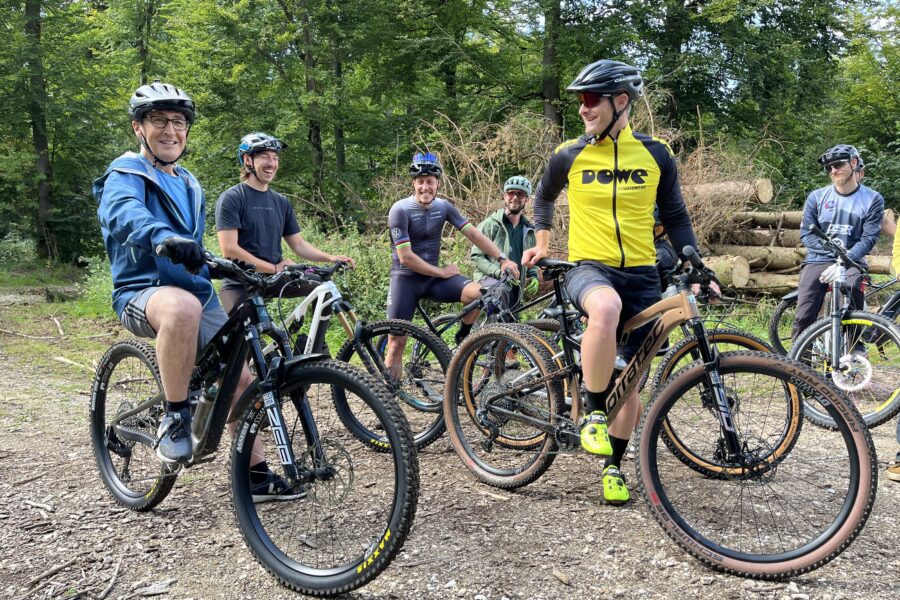 Sechs Personen mit Fahrrädern im Wald, lächelnd und in Sportkleidung.