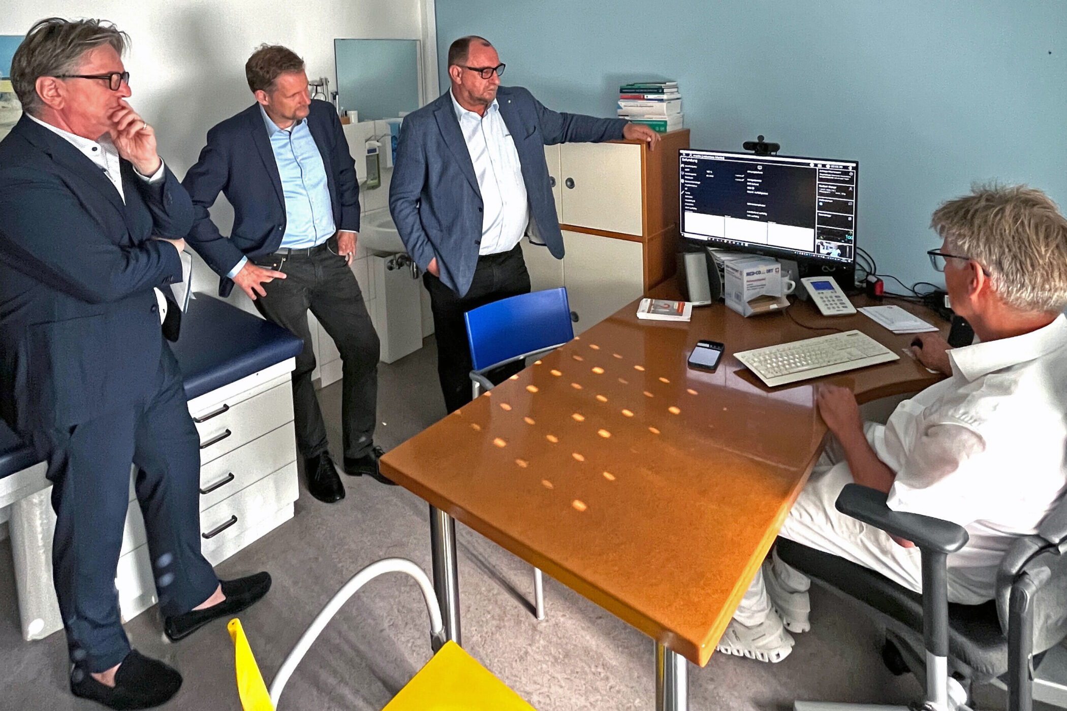 Fünf Männer in einem Büro, einer sitzt am Schreibtisch, vier stehen daneben.