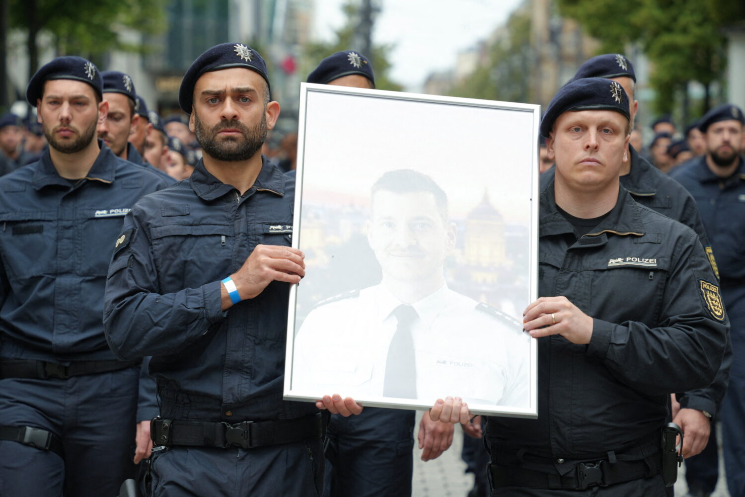 Zwei Polizisten in Uniform tragen ein gerahmtes Foto, weitere Polizisten im Hintergrund.