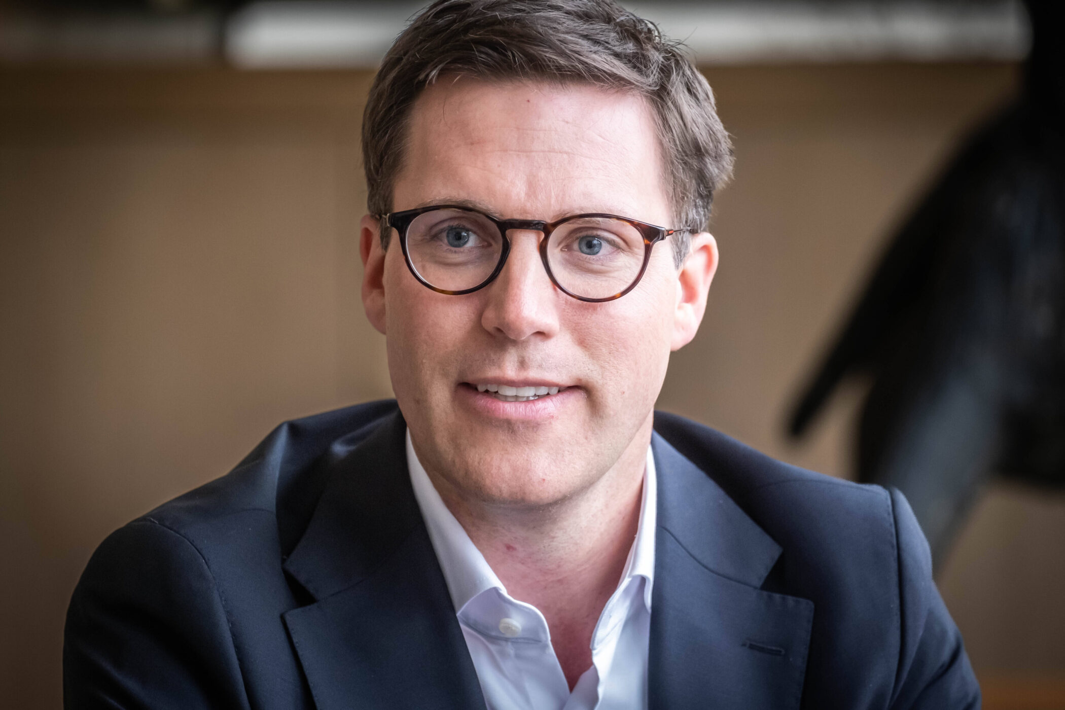 Ein Mann mit Brille und Anzug lächelt in die Kamera.