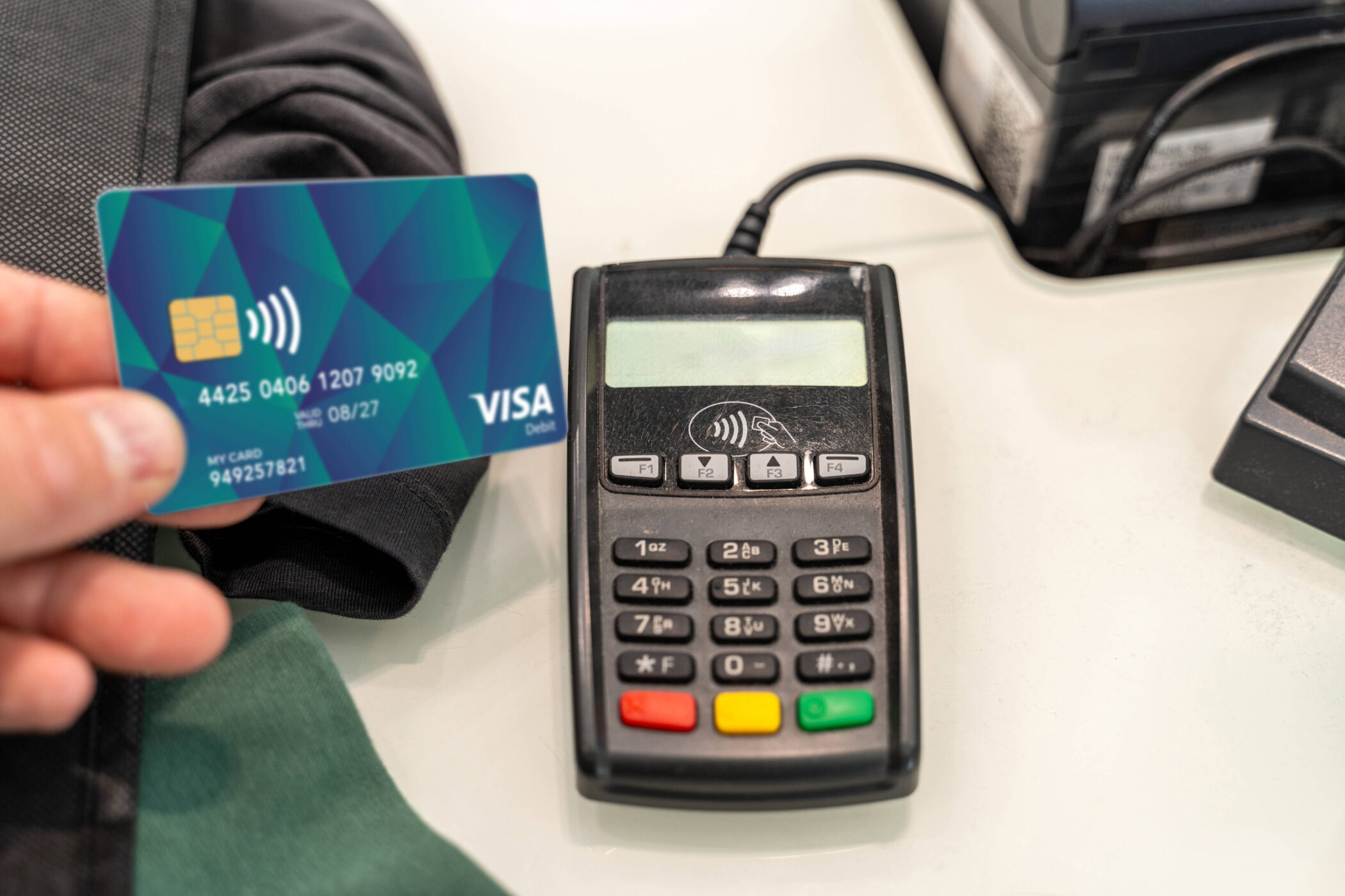 Hand hält Kreditkarte vor Kartenlesegerät auf einem Tisch.