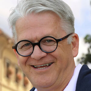 Ein lächelnder Mann mit Brille und grauen Haaren.