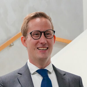 Ein Mann mit Brille und Anzug lächelt in die Kamera.