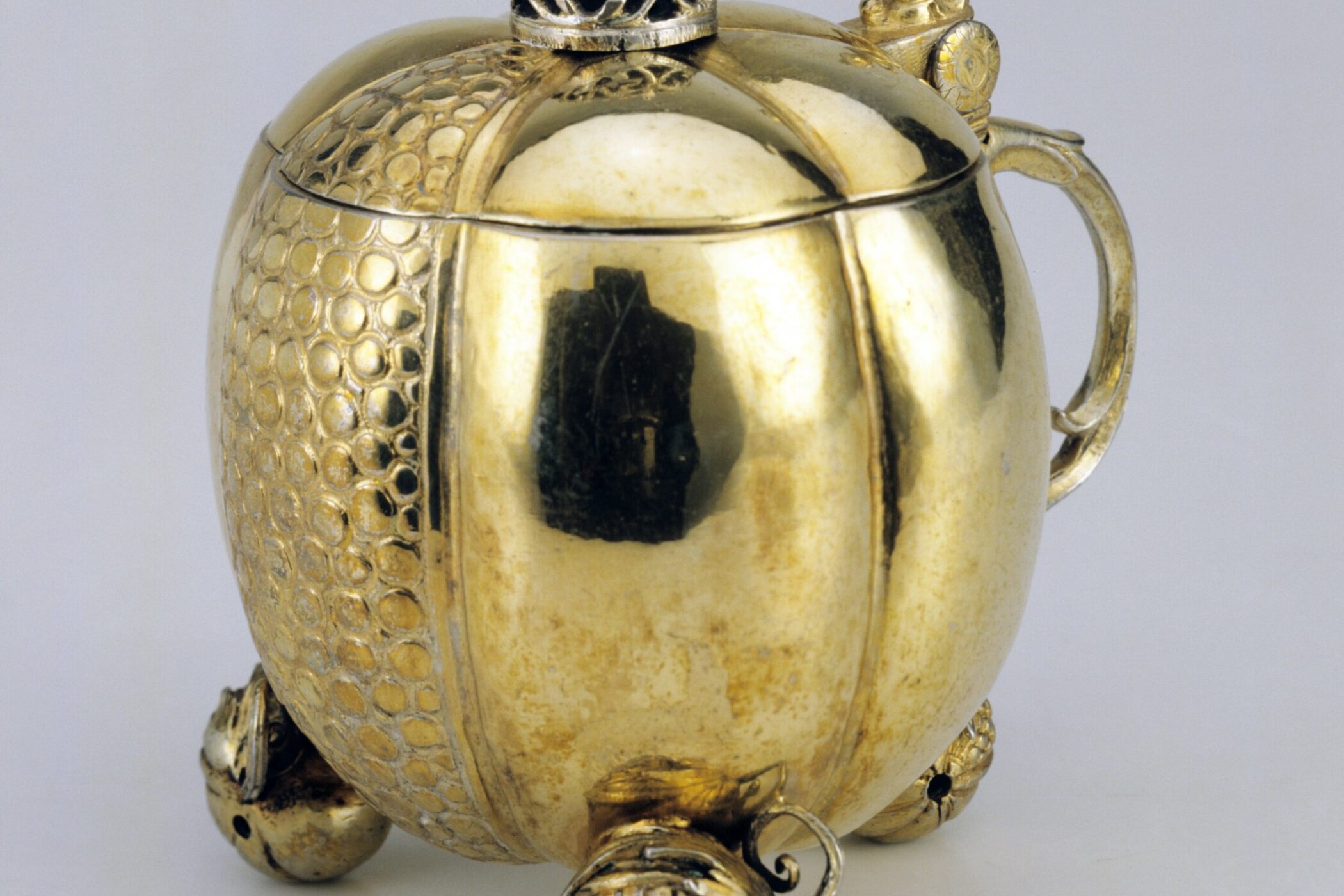 Goldene Teekanne mit Krone auf dem Deckel, verziert mit Reliefmustern und Figuren.