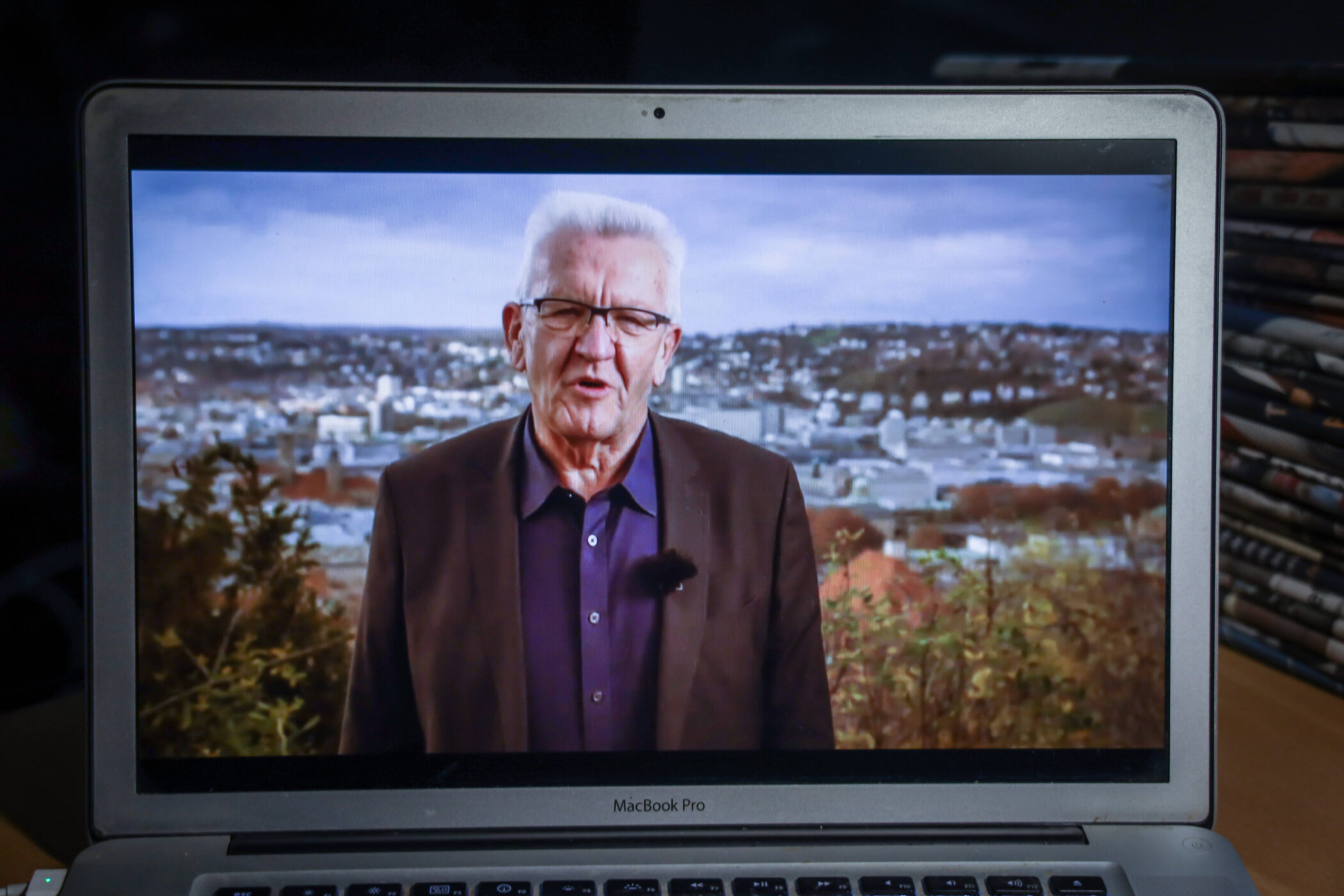 Älterer Mann spricht auf einem Laptop-Bildschirm, Stadt im Hintergrund.