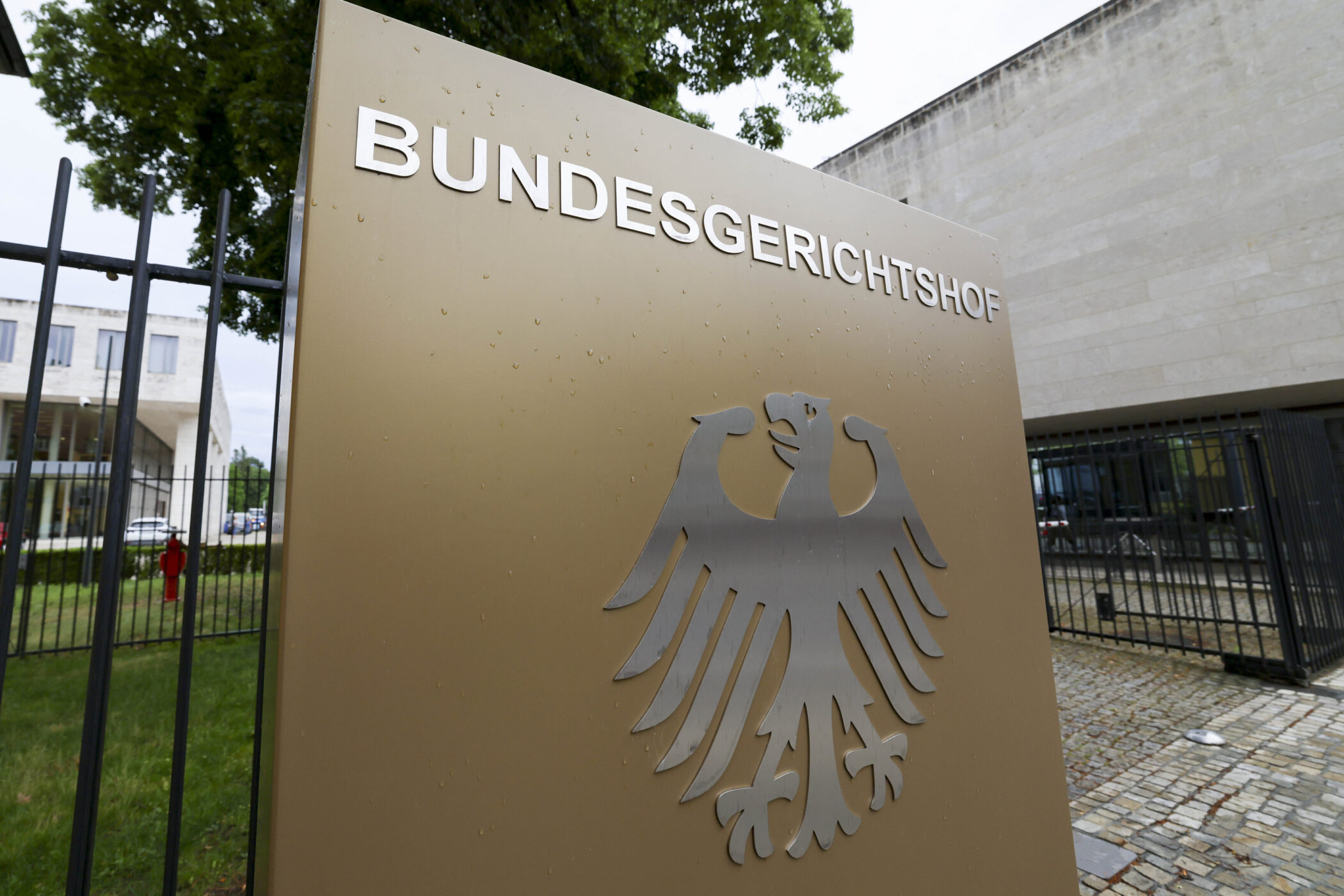 Schild mit Aufschrift "BUNDESGERICHTSHOF" und Bundesadler, Gebäude im Hintergrund.