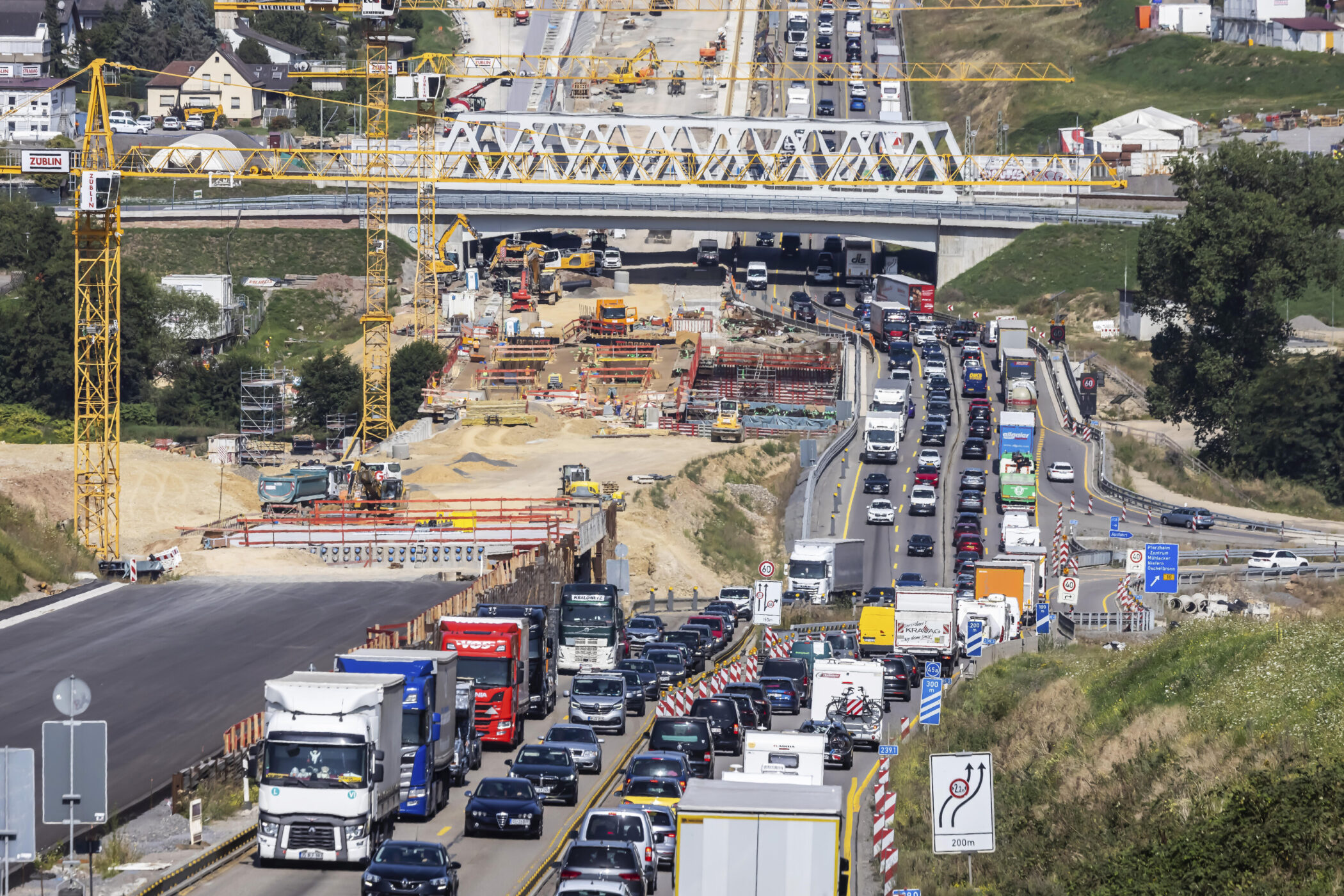 Verkehrsstau auf Autobahn, Baustelle mit Kränen und Brücke im Hintergrund.