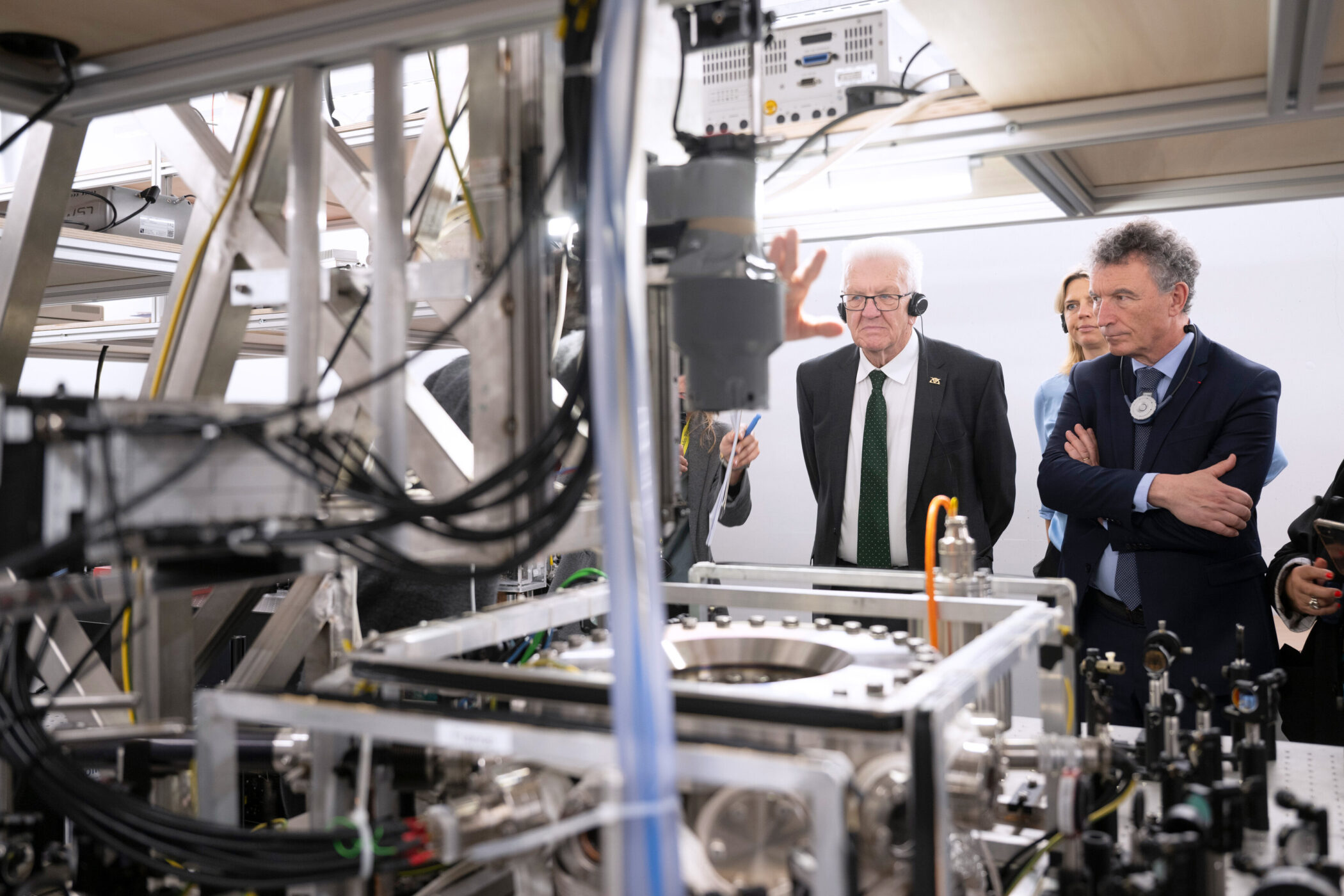 Drei Personen mit Headsets betrachten eine technische Anlage in einem Labor.